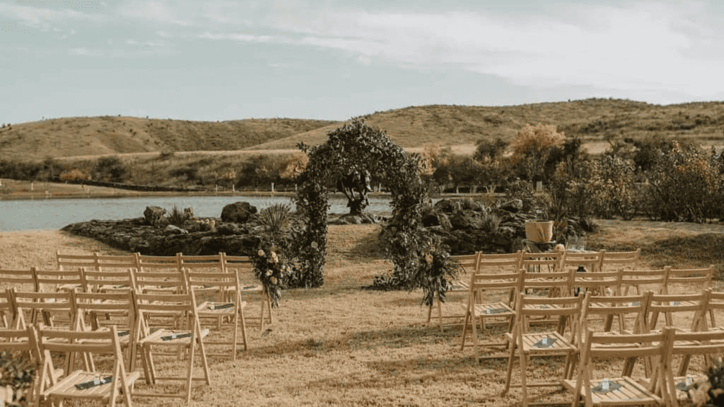 lakeside wedding ceremony setup with wooden chairs and arch